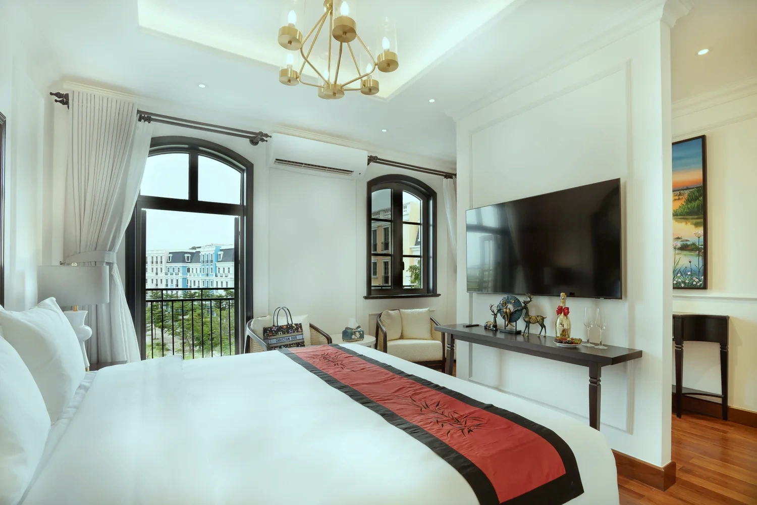 La Rose Suite bedroom with arched French windows looking out towards Sunset Town, a brass chandelier and a red bamboo-motif runner